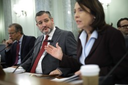 Sen. Ted Cruz, R-Texas, is pictured sitting behind a desk at a Senate Commerce hearing. He's looking at Chair Maria Cantwell, D-Wash., who is sitting next to him and speaking into a microphone.