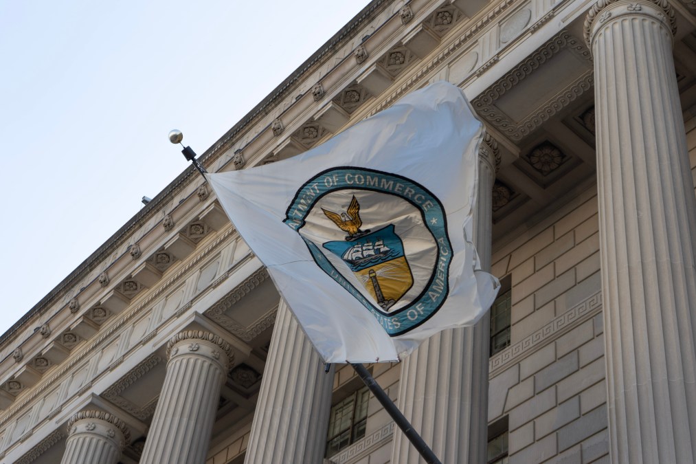 The circular Department of Commerce seal appears on a white flag attached to the front of the agency's federal-style building. The flag blows in the wind, displaying a majority of the seal.