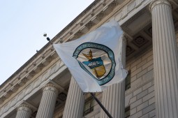 The circular Department of Commerce seal appears on a white flag attached to the front of the agency's federal-style building. The flag blows in the wind, displaying a majority of the seal.